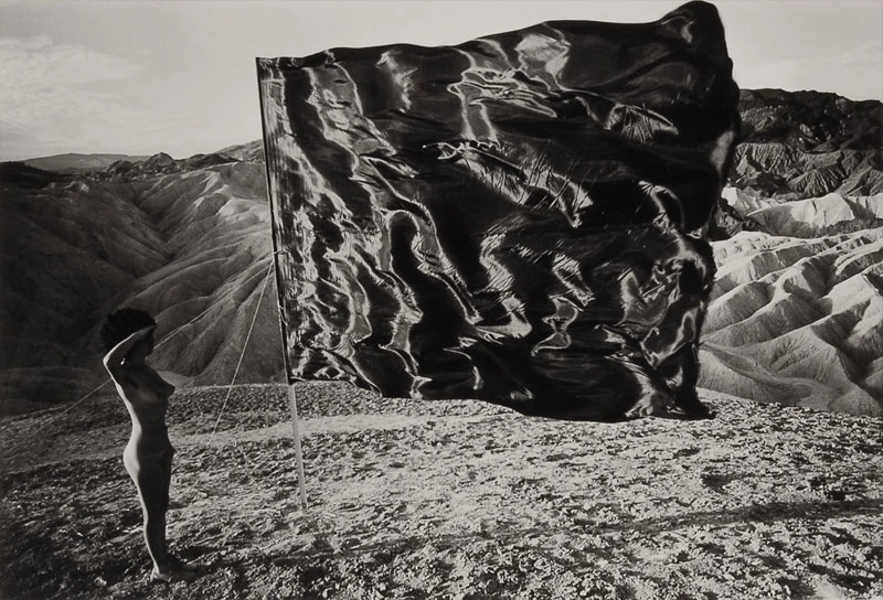 A young naked girl standing near a black flag in the desert. Photo by Ettore Sottsass