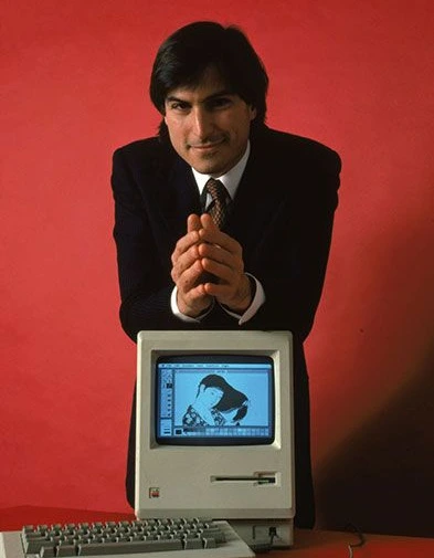 Young Steve Jobs on a red background with a Macintosh computer