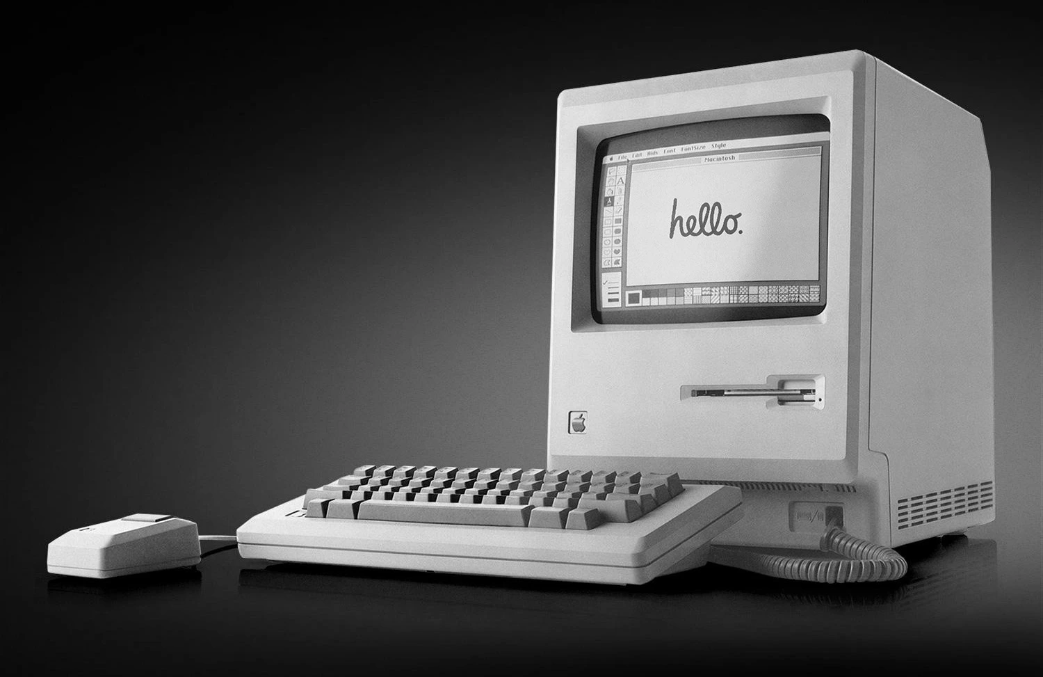 The first Macintosh computer. Mouse, keyboard and monitor with a word Hello written on the screen