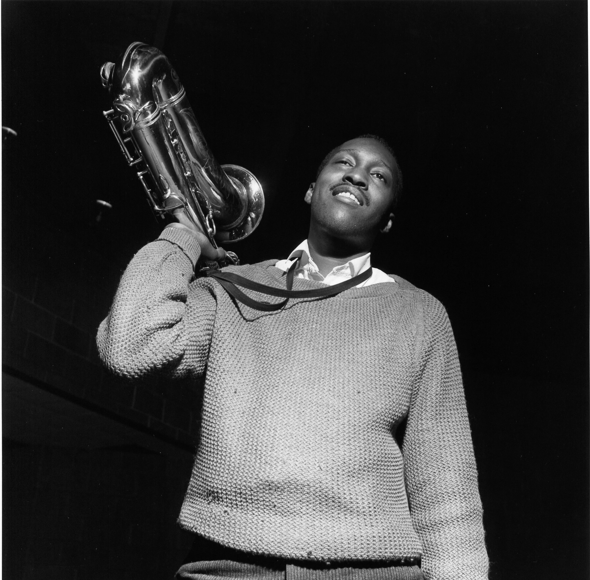 Hank Mobley smiles holding a saxophone in his right arm during his Soul Station session