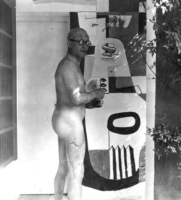 Naked Le Corbusier painting one of his murals at Eileen Gray&#x27;s E-1027, looking into camera