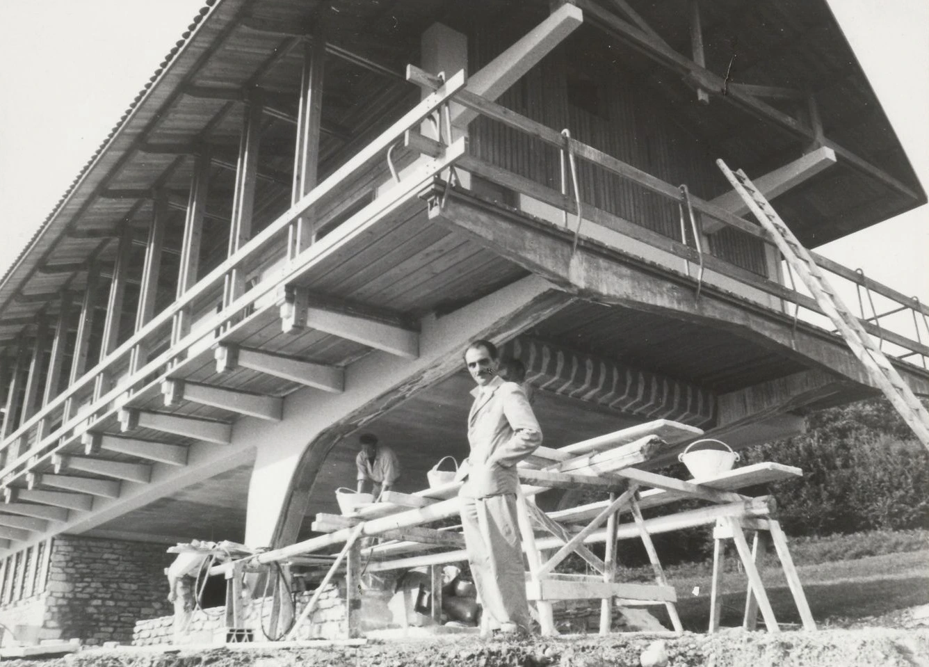 Carlo Mollino in front of a massive wooden house in Turin