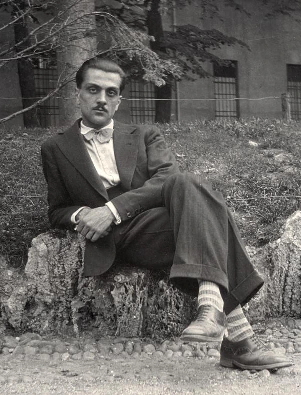 Carlo Mollino sitting on the road side, looking at the camera