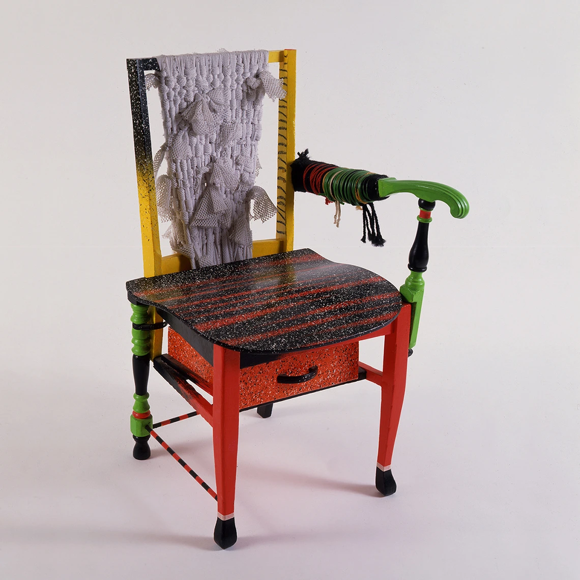 A red, green, yellow, grey and black armchair with one arm and a drawer under the seat