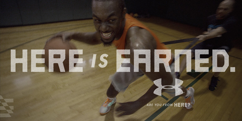 An ad for the brand Under Armour highlighting their basketball division. The ad features Kemba Walker aggressively training and pulling his trainer who has a band around his waist. The headline "Here is Earned" is over the image with the tagline: Are you from Here? underneath.