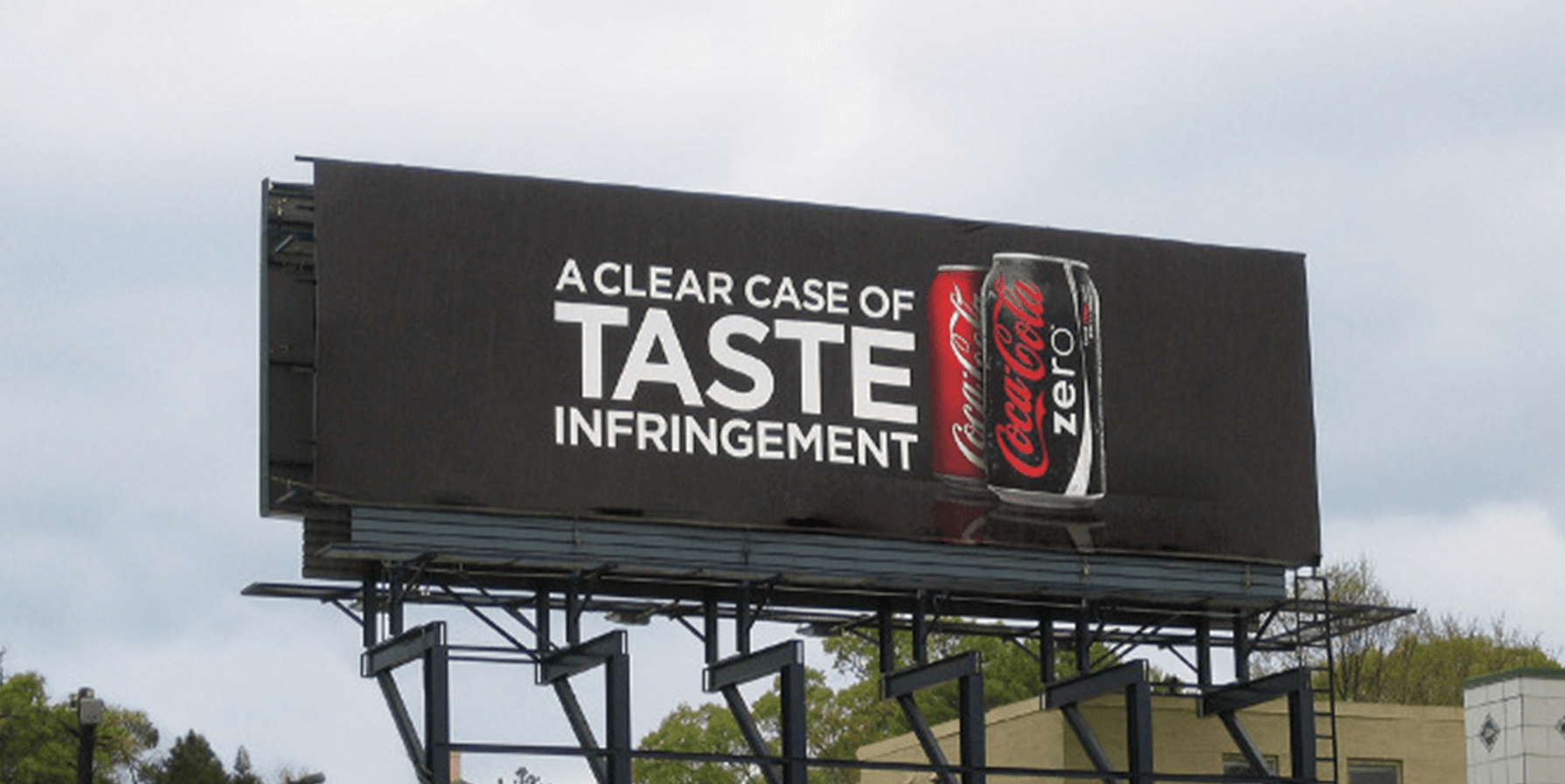 An OOH Billboard for the launch of Coke Zero. It shows the Coke Zero can in front of a Coca-Cola can. The headline reads, "A Clear Case of Taste Infringement" This alludes to the fact that Coke Zero tastes enough like Coke that you could sue.