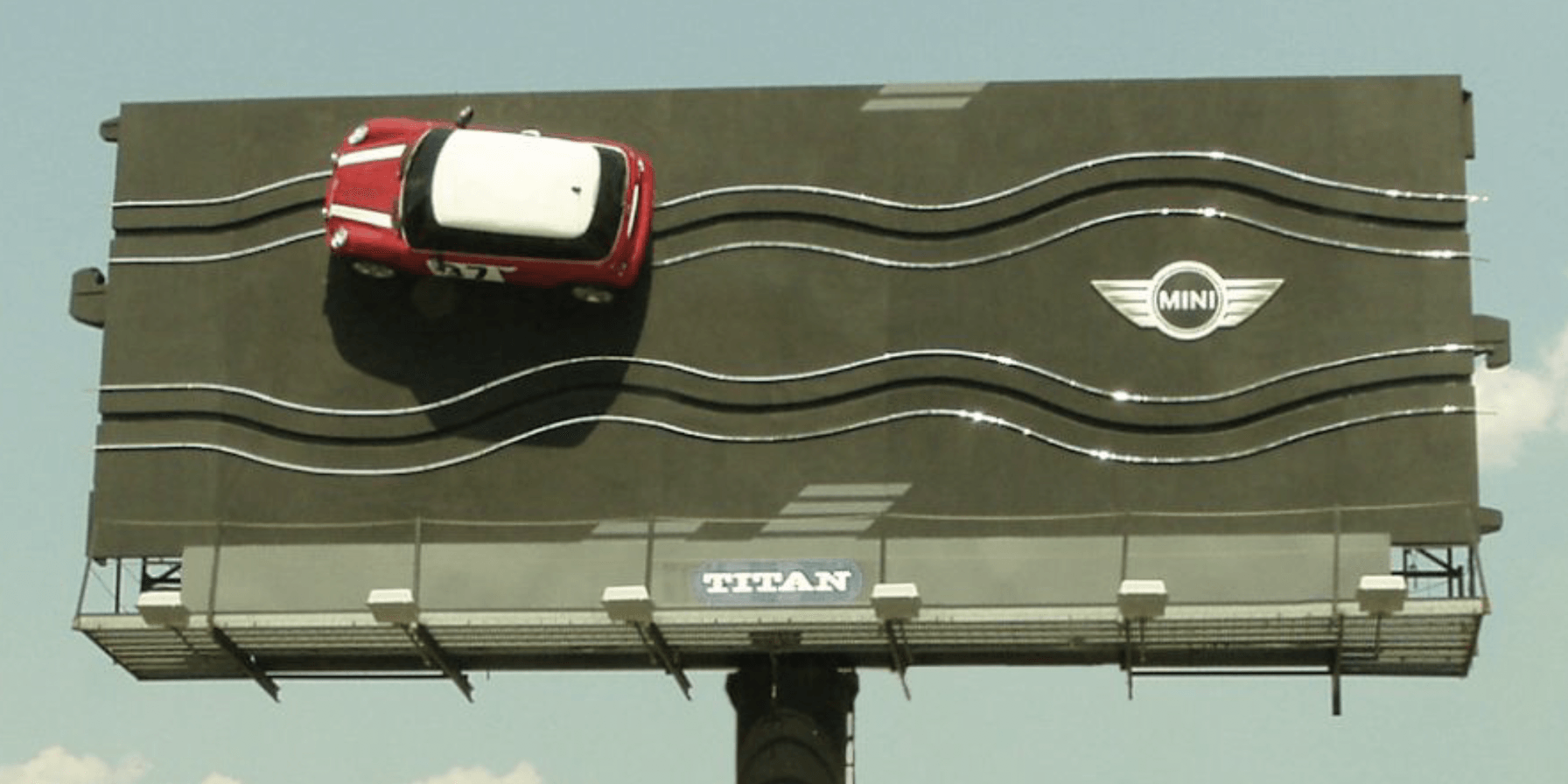An OOH billboard for MINI Cooper that reworks the shape of the billboard to resemble a child's car racing track. The line is swerving with a giant MINI Cooper attached to the track piece.