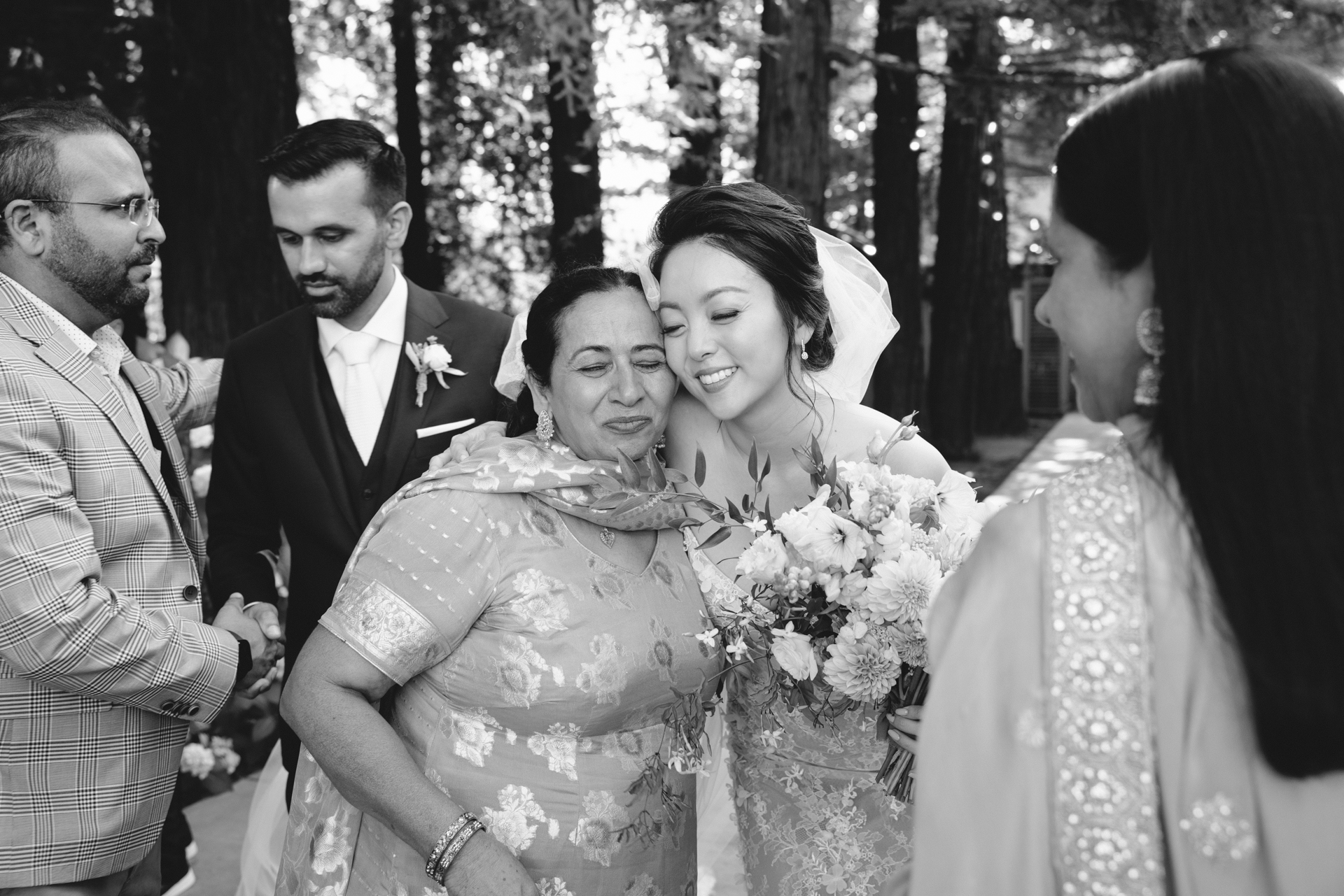 Emotional candid photograph of the bride and groom hugging family members on their wedding day.