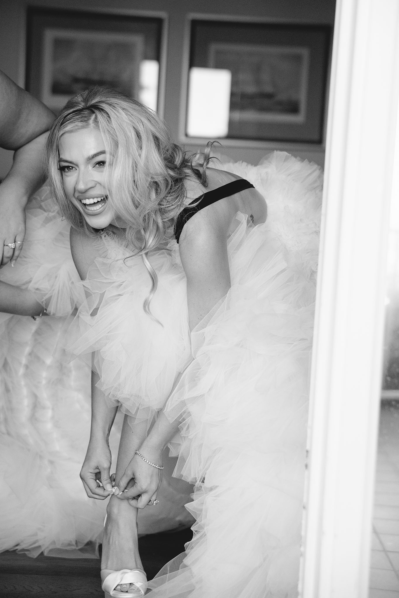Candid photo of bride laughing while she is putting on her shoe in her couture wedding dress on her wedding day. San Diego Wedding Photographer.