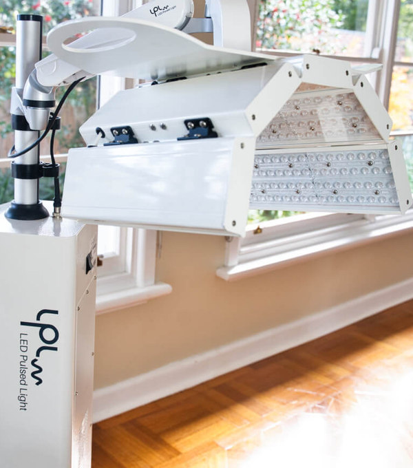 An LED Pulsed Light machine standing in a room with wooden floorboards and sash windows in the background