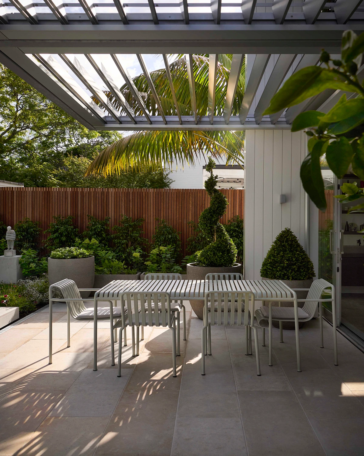 Parnell Courtyard: an outdoor dining table under a glazed pergola, with clipped planting and a timber fence