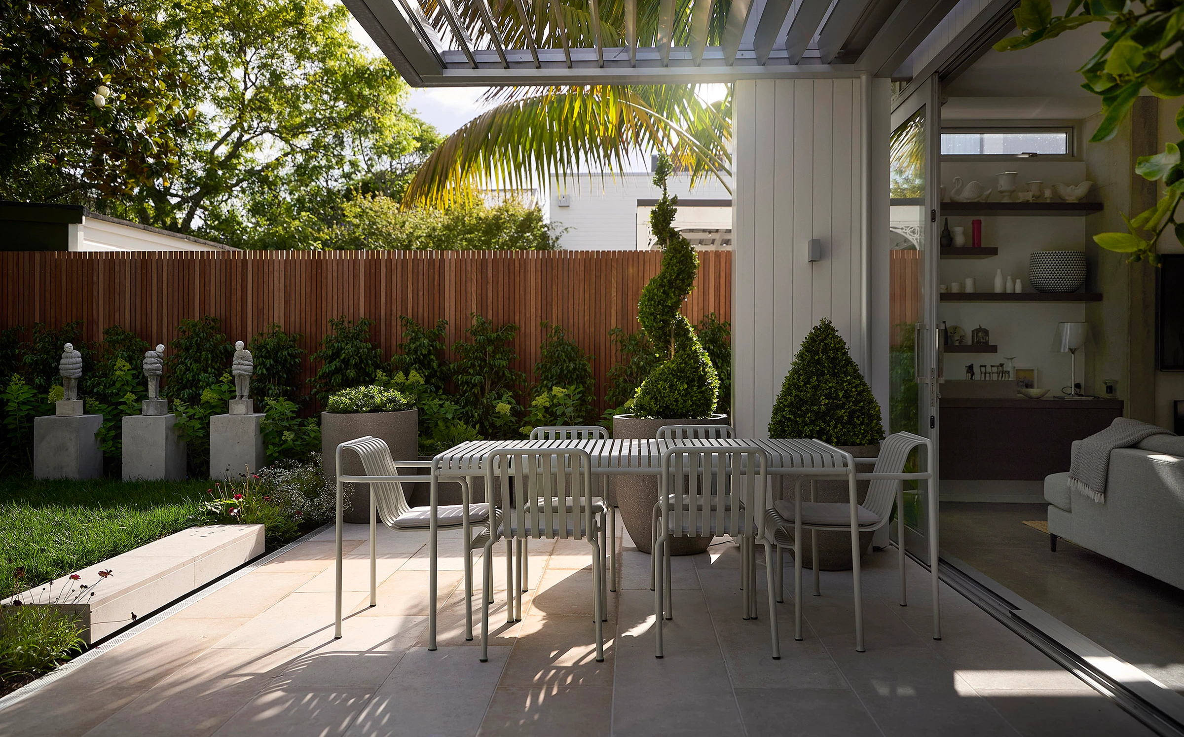 Parnell Courtyard: an outdoor dining table under a glazed pergola, with clipped planting and a timber fence