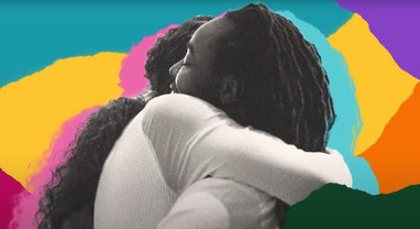 Two Black, trans figures embrace, with a collage of brightly colored paper scraps as their background.