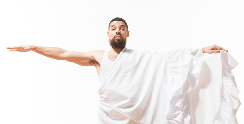 A light skinned Black femme with short black hair in a white undershirt and long white skirt is shown from the waist up, caught in mid motion with the skirt tossed over their left arm.
