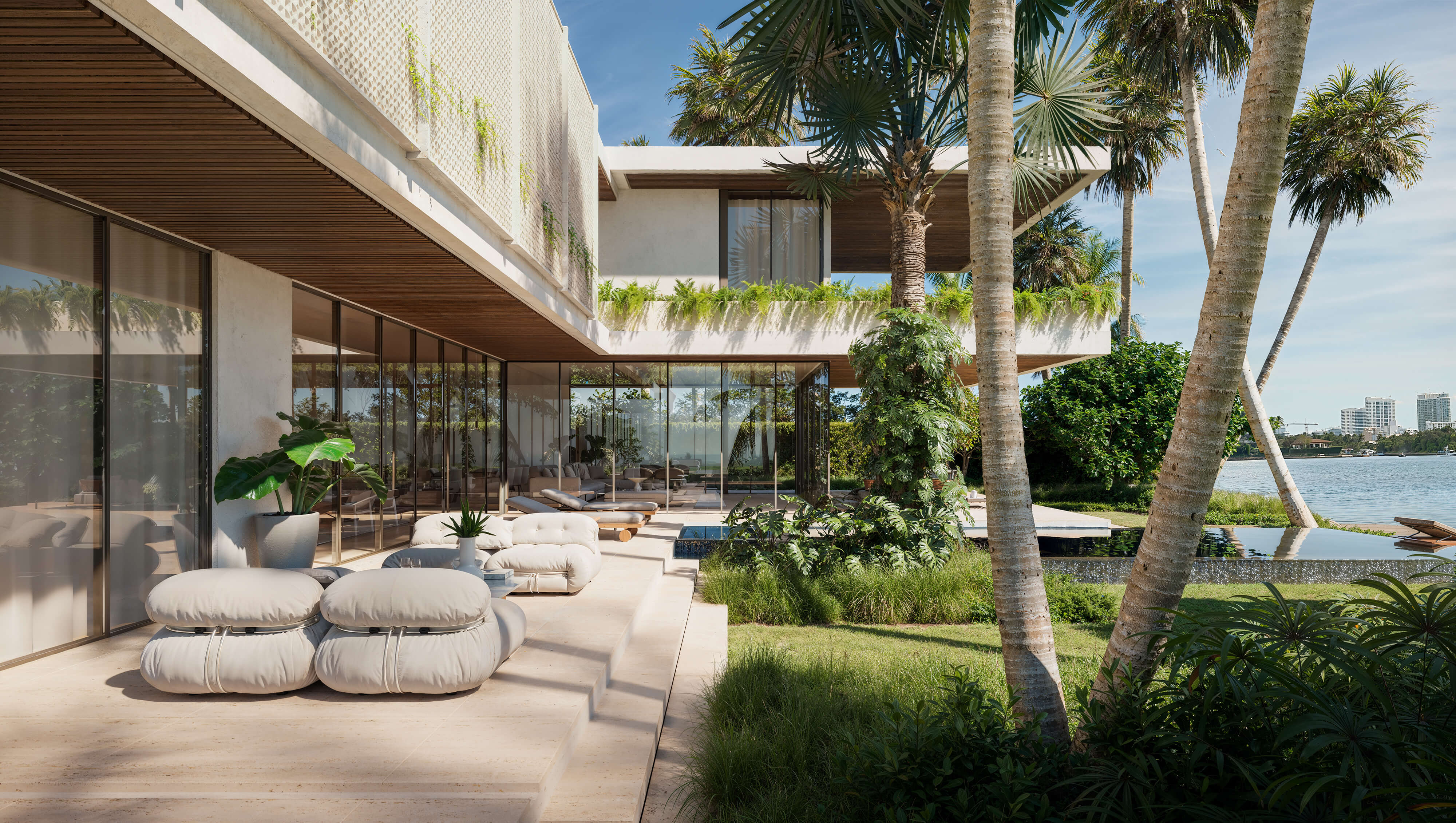 Exterior 3D render of Bay House, a modern waterfront residence with tropical landscaping, glass walls, outdoor lounge furniture, and views of the bay; designed for KoDA, USA, 2024.