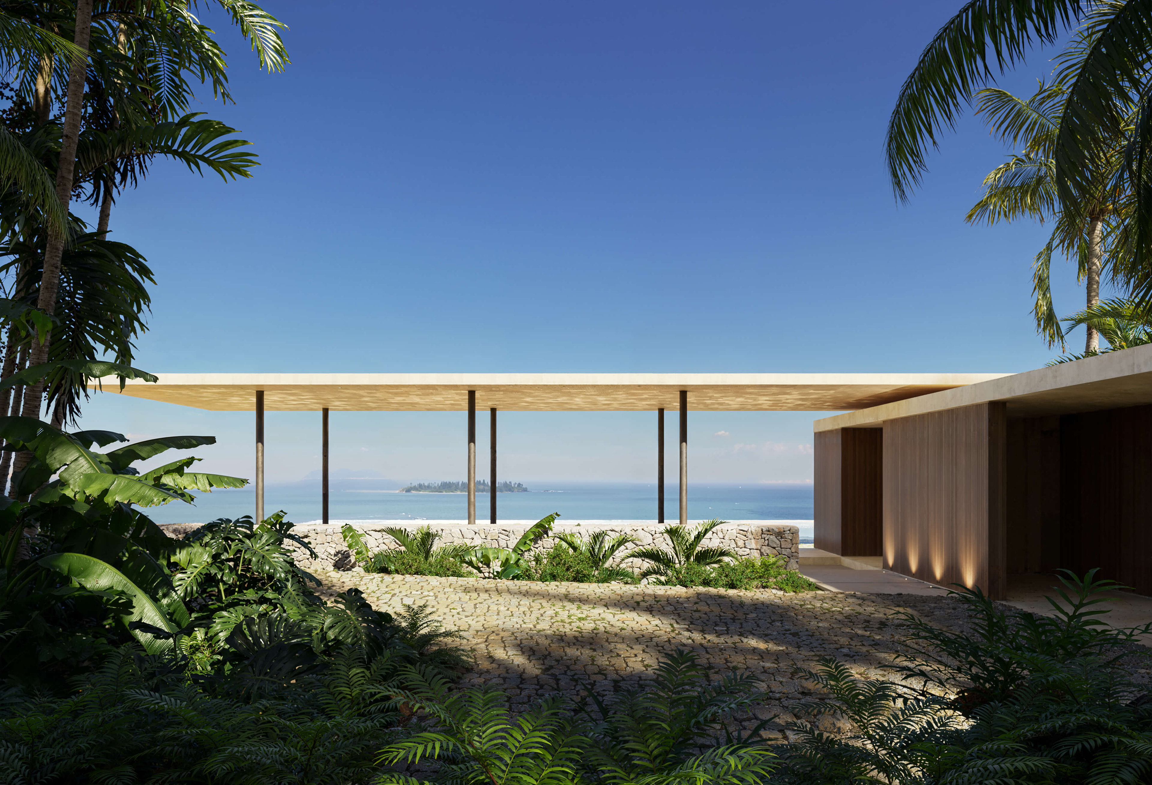 Daytime CGI of Puerto Rico Residences, 2024 by KoDA, USA — minimalist coastal home with stone pathway, tropical landscaping, and open pavilion roof framing ocean views and a distant island.