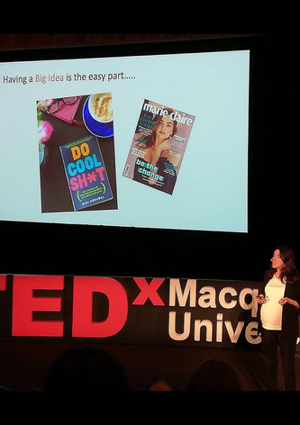 Dr Melina Georgousakis presenting on stage at a TEDx event, standing beside a large screen displaying slides with the heading “Having a Big Idea is the easy part…”.