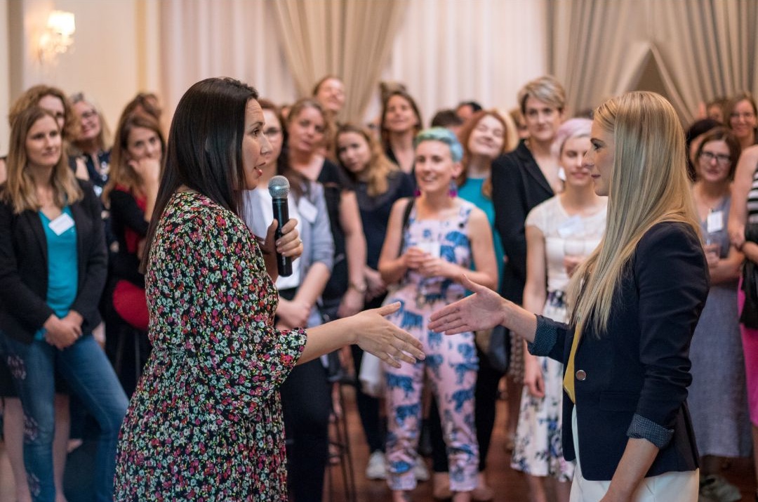 Women attending a Franklin Women networking event, with two participants speaking into a microphone and greeting each other while others look on.