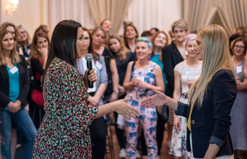 Women attending a Franklin Women networking event, with two participants speaking into a microphone and greeting each other while others look on.