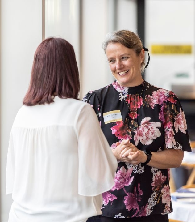 Two Franklin Women members engaged in conversation at an event, smiling and speaking together in a bright venue.