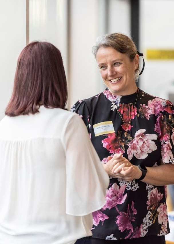 Two Franklin Women members engaged in conversation at an event, smiling and speaking together in a bright venue.