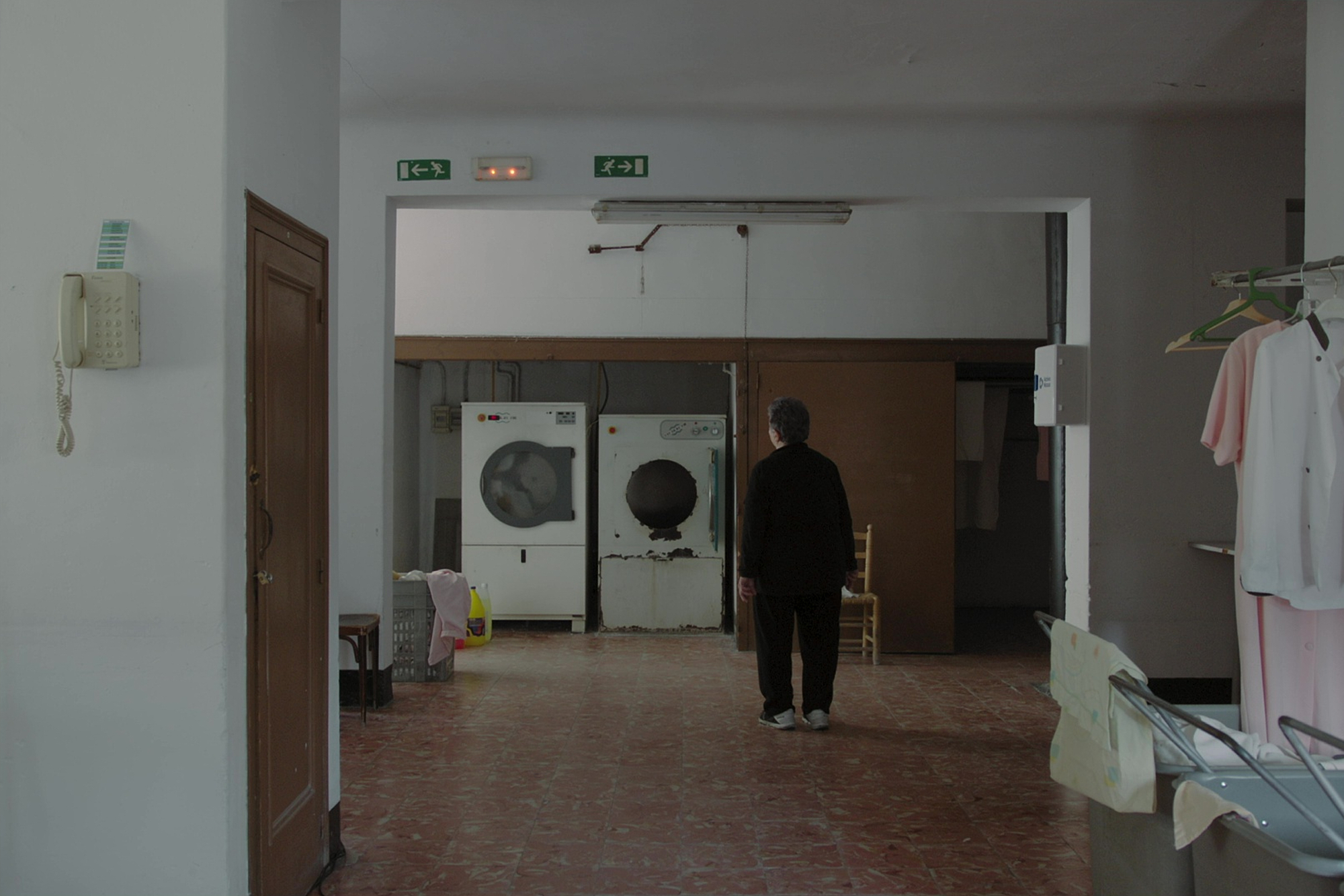Film still from La Panadella of a woman watching a laundry machine spin, her gaze fixed on the rotating drum