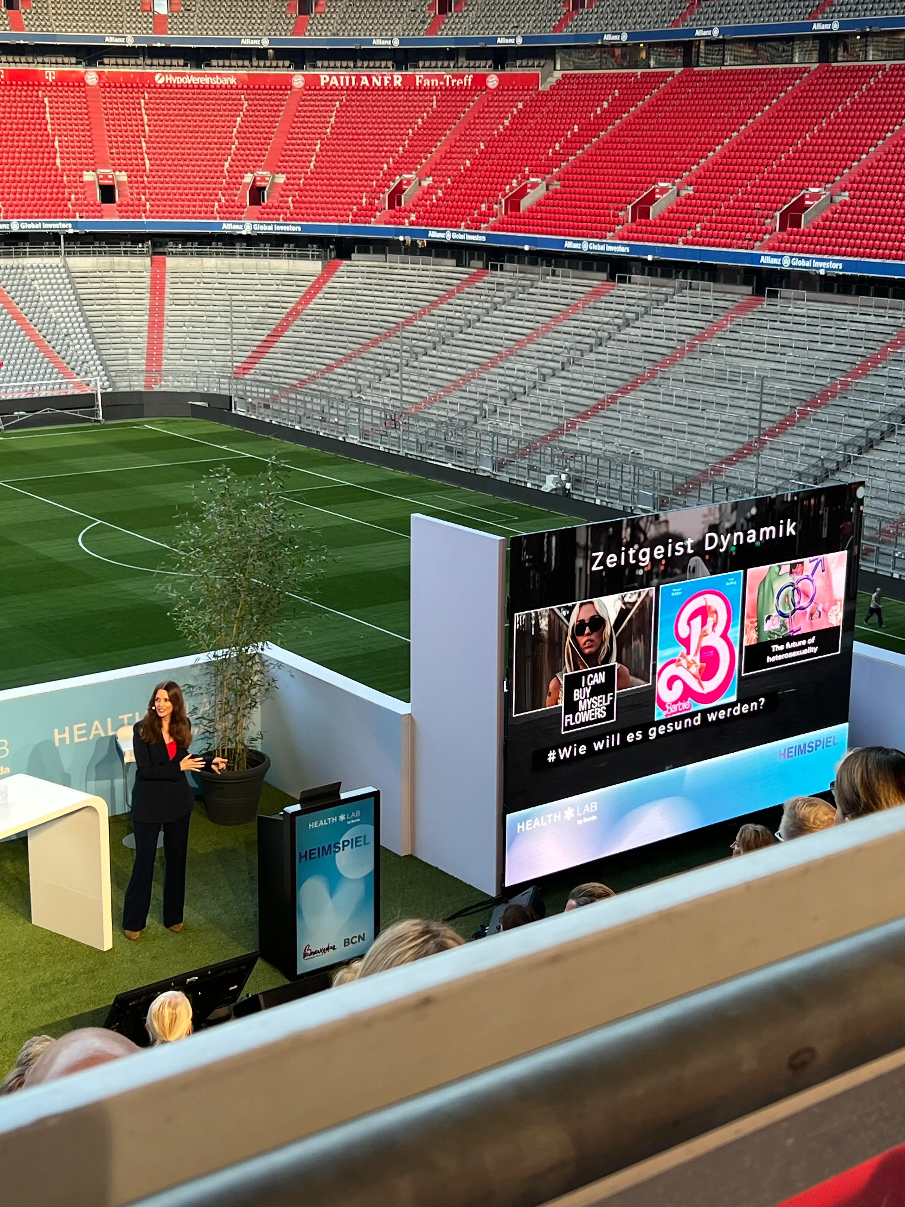 Kirstine Fratz spricht vor Publikum in einem Stadion, im Hintergrund eine Leinwand mit der Aufschrift 'Zeitgeist Dynamik'
