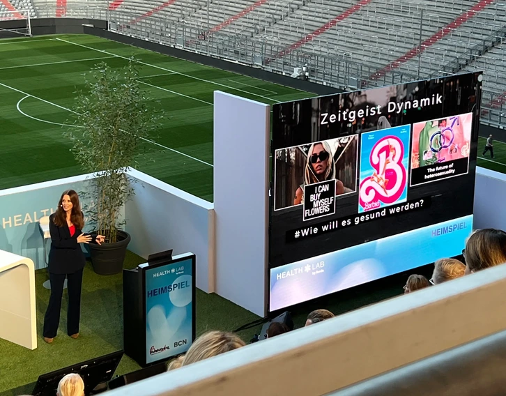 Kirstine Fratz spricht vor Publikum in einem Stadion, im Hintergrund eine Leinwand mit der Aufschrift 'Zeitgeist Dynamik'