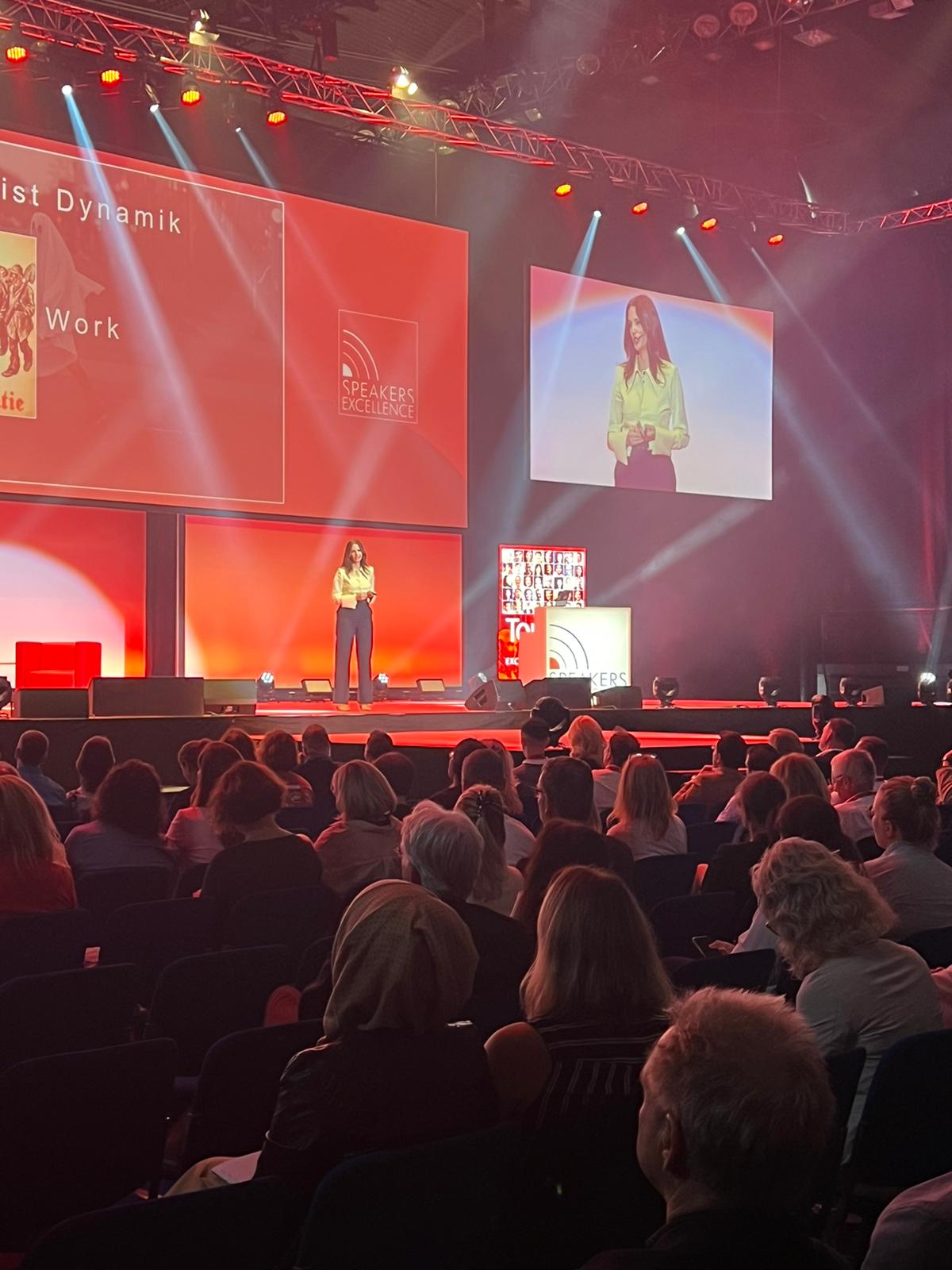 Kirstine Fratz hält eine Keynote vor großem Publikum, im Hintergrund eine Präsentationsfolie zu 'Zeitgeist Dynamik'