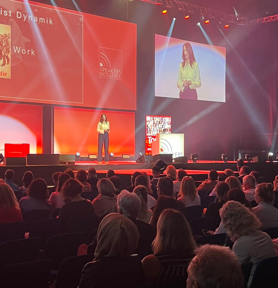 Kirstine Fratz hält eine Keynote vor großem Publikum, im Hintergrund eine Präsentationsfolie zu 'Zeitgeist Dynamik'