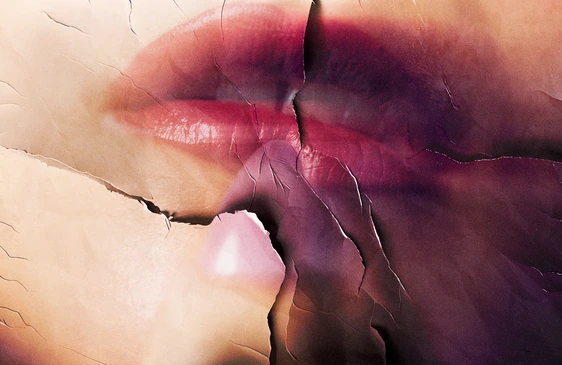 Close-up colour photograph of two faces in profile meeting for a kiss, with soft skin tones and deep magenta and burgundy shadows creating depth and intimacy.